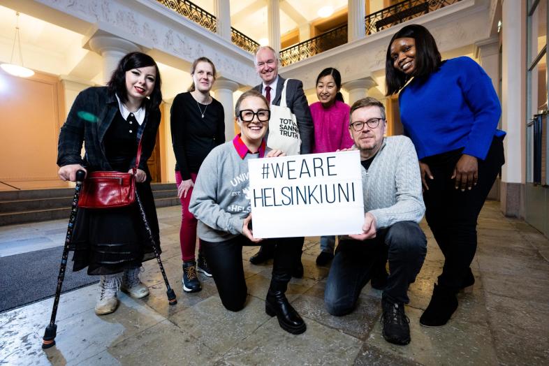 Yliopistolaisia päärakennuksen aulassa #wearehelsinkiuni-kyltin kanssa.