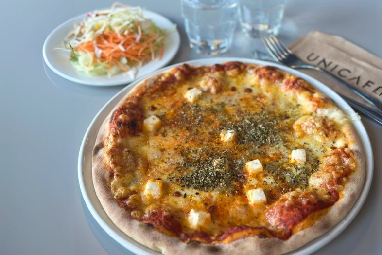 Lautasella pizza, taka-alalla raastelautanen, vesilaseja haarukka.