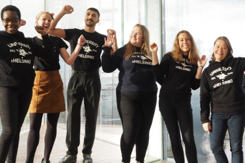 Iloiselta näyttävä ryhmä nuoria ihmisiä poseeraa Oodi kirjaston sisäikkunan edessä