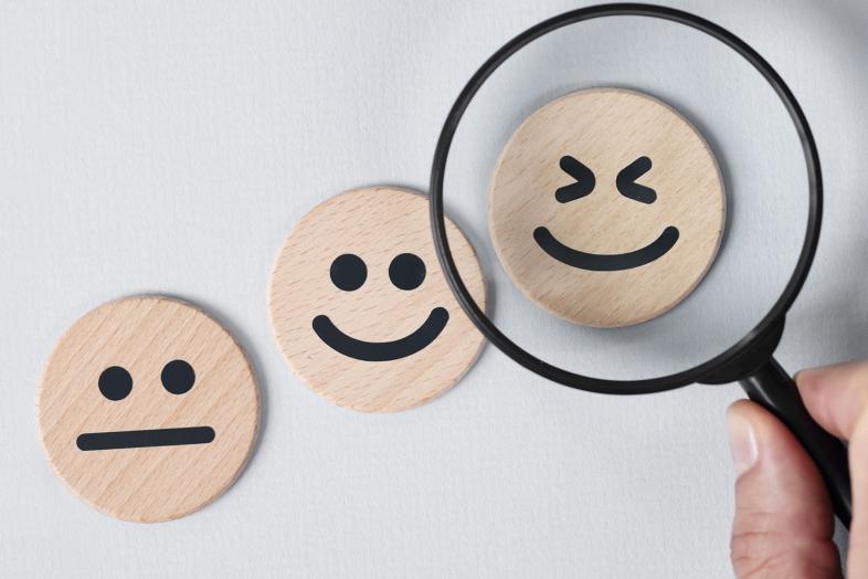 Kolme hymyilevää puupalikkaa ja suurennuslasi, joka osoittaa leveimmin hymyilevää puupalikkaa.