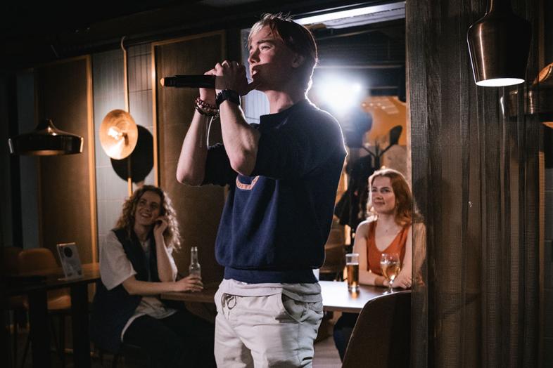 Etualalla karaokelaulaja, taustalla yleisöä pöydän ääressä.