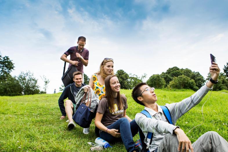 Ryhmä opiskelijoita ottaa selfietä nurmikentällä.