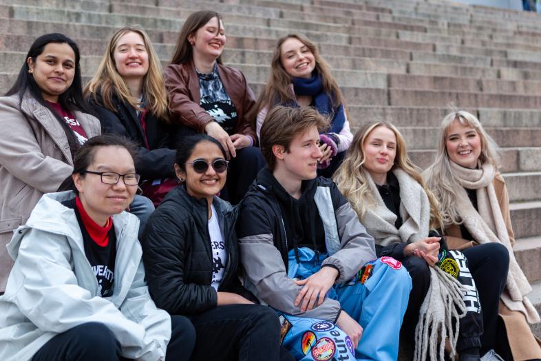 Iso ja iloinen ryhmä opiskelijoita istuu Tuomiokirkon portailla