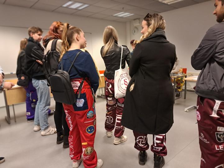 Ryhmä haalareihin pukeutuneita opiskelijoita luentosalissa.