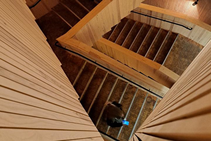 Henkilö kävelee alas Tiedekulman mutkikasta puista rappukäytävää matkapuhelin kädessä.