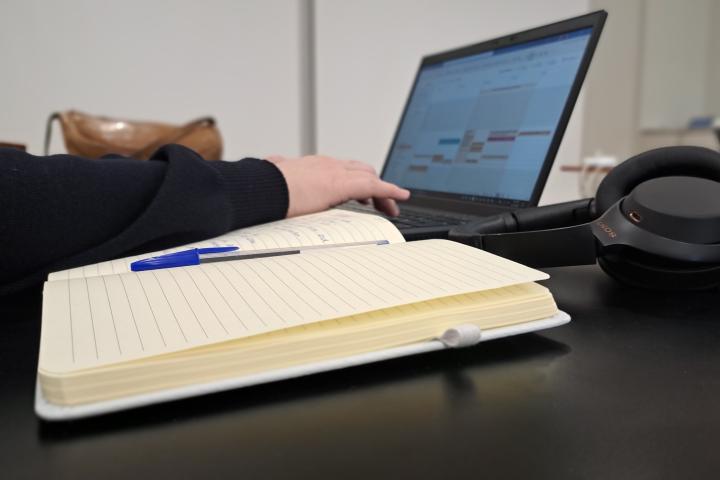 Etualalla muistivihko, taustalla kuulokkeet ja kannettava tietokone.
